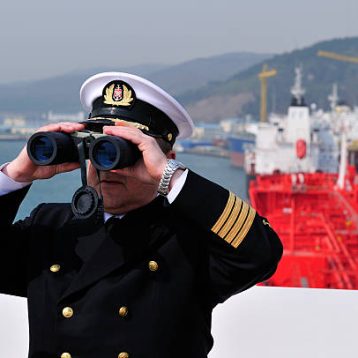 Navigation officer with binocular, looking ahead on the navigation bridge of ocean ship
